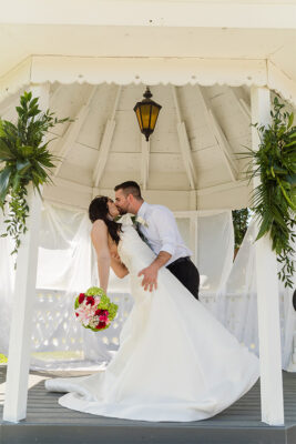 Groom dipping bride inside gazebo for a kiss