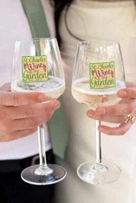 Bride and groom holding wine glasses with St. Charles Wine garden logo